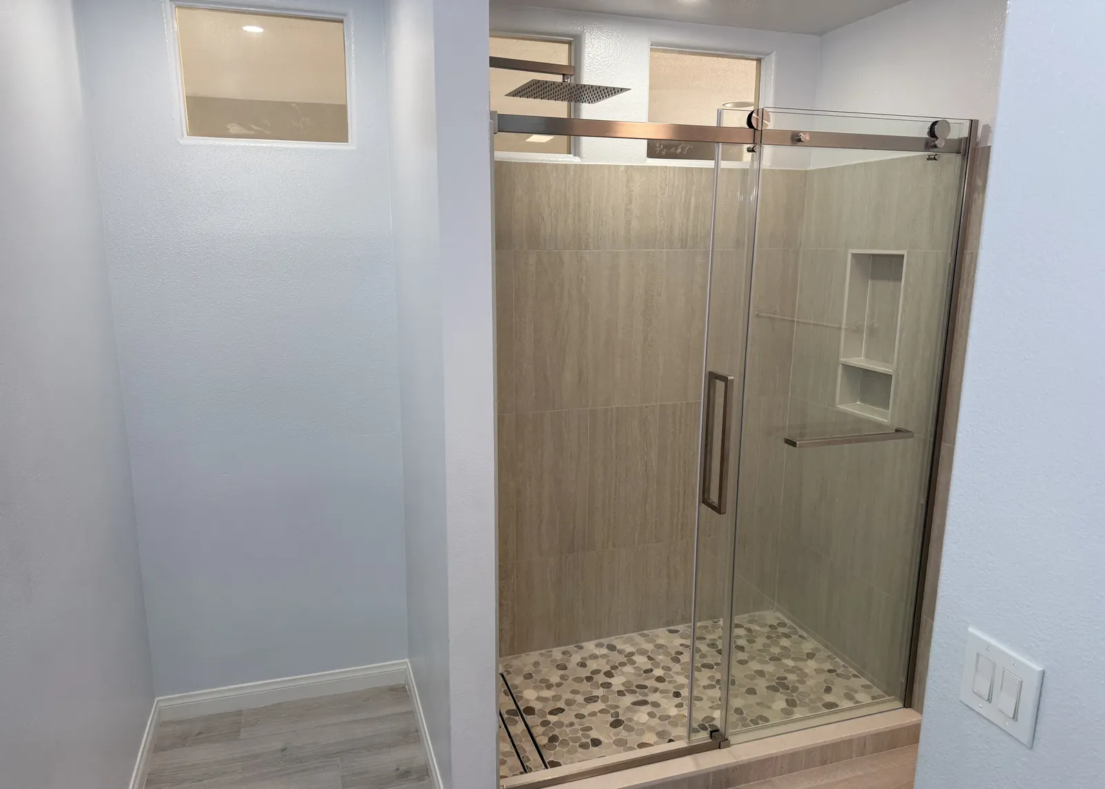 New walk-in shower with a frameless sliding glass door, pebble tile floor, recessed niche and rain shower head