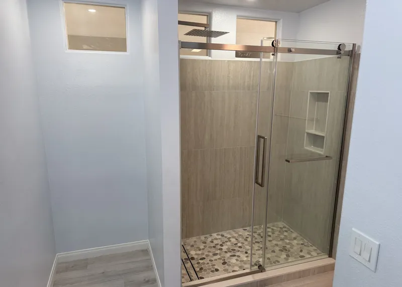 New walk-in shower with a frameless sliding glass door, pebble tile floor, recessed niche and rain shower head