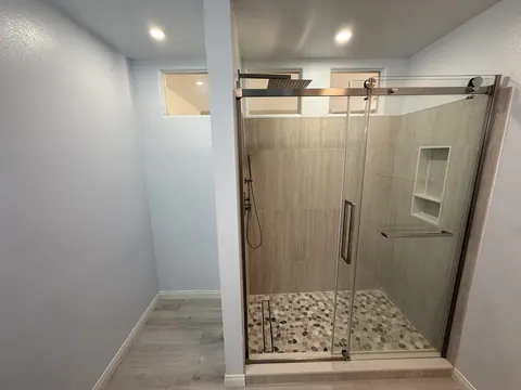 Finished walk-in shower with a frameless sliding glass door, pebble tile floor, tiled niche, rain head and handheld sprayer