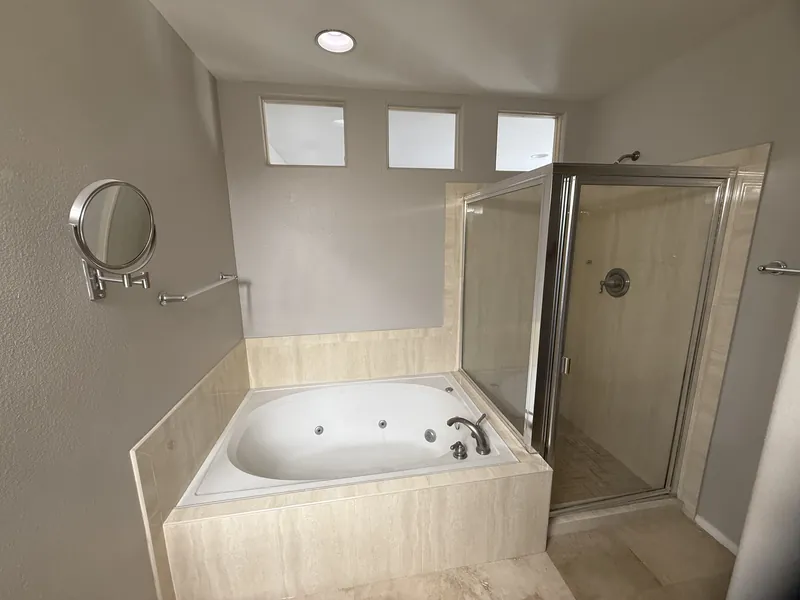 Bathroom before the remodel with a beige tile jetted tub under three small windows and a corner shower with a framed door