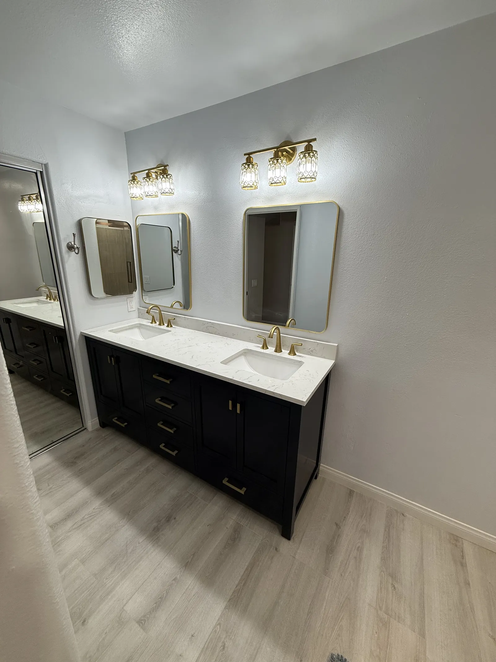 Finished black double vanity with a white veined countertop, gold faucets, gold framed mirrors and matching light fixtures
