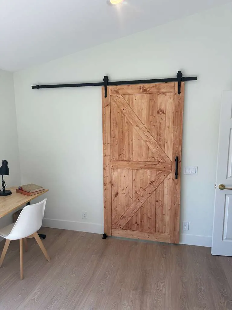 Knotty wood sliding barn door on black track hardware closed across the bathroom opening in the bedroom
