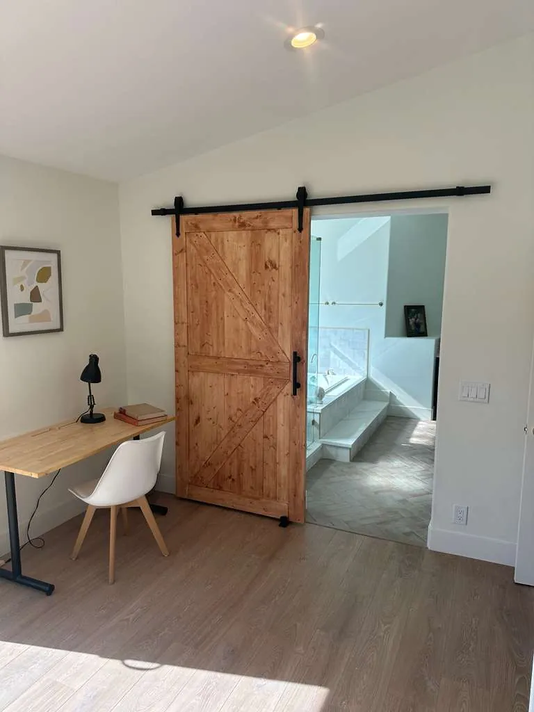 Sliding barn door rolled open to reveal the tiled tub deck and herringbone floor of the primary bathroom