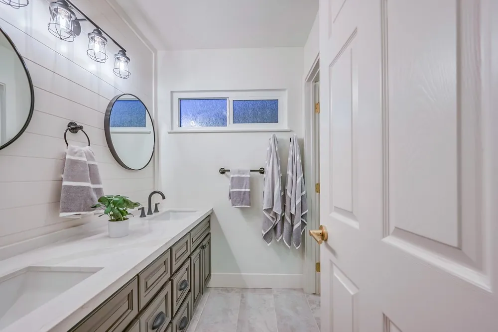 Bathroom with a gray-green vanity, marble-look counter, round mirrors on a shiplap wall and black cage sconces