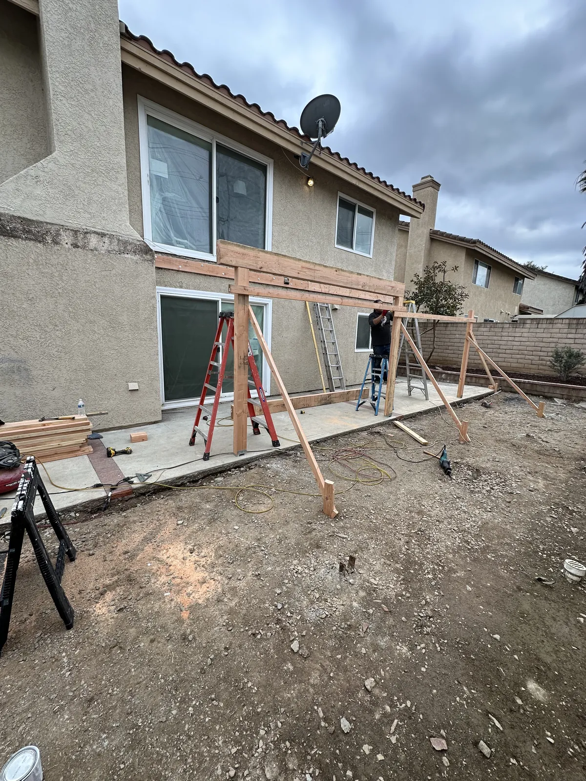 Posts and beams of the new backyard deck going up against the back of a two-story house