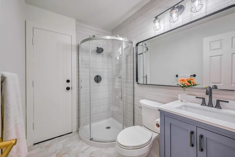 Finished bathroom with a curved glass corner shower, gray vanity, black fixtures and marble-look tile floor