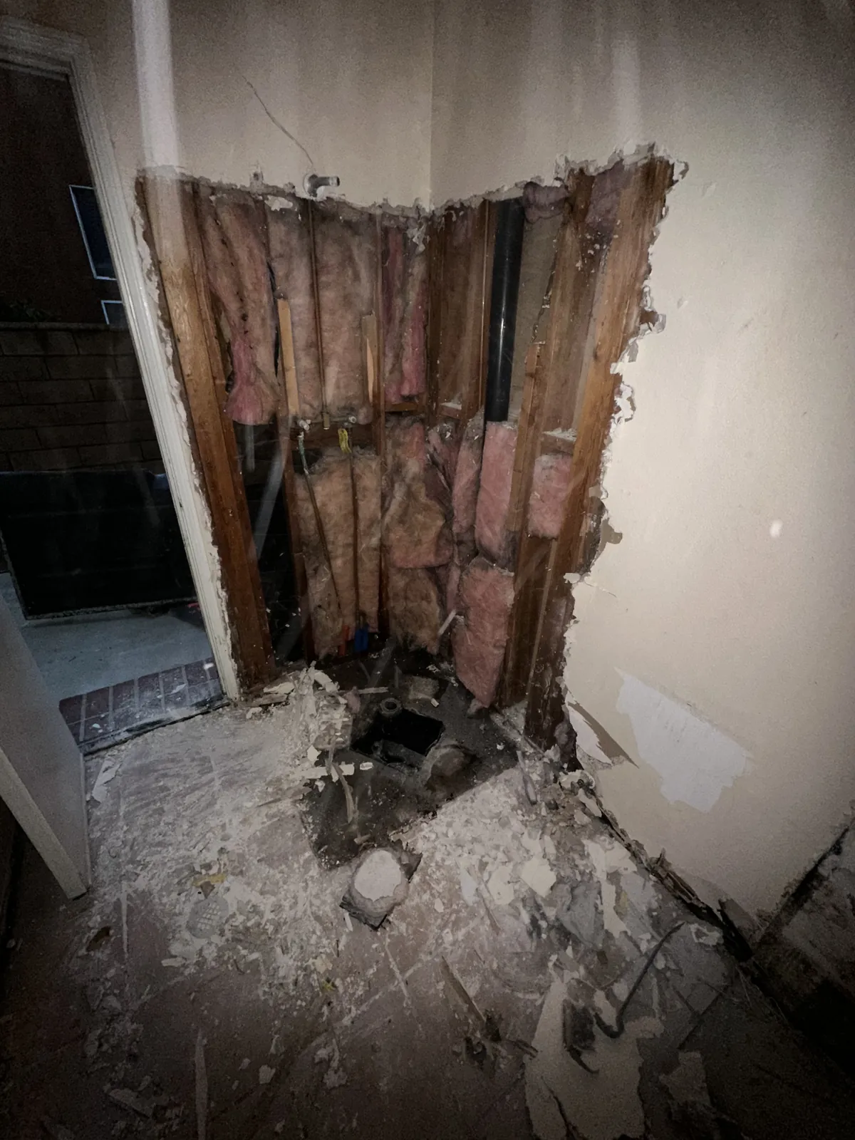 Shower corner stripped to the studs with insulation exposed and the drain opened up during demolition