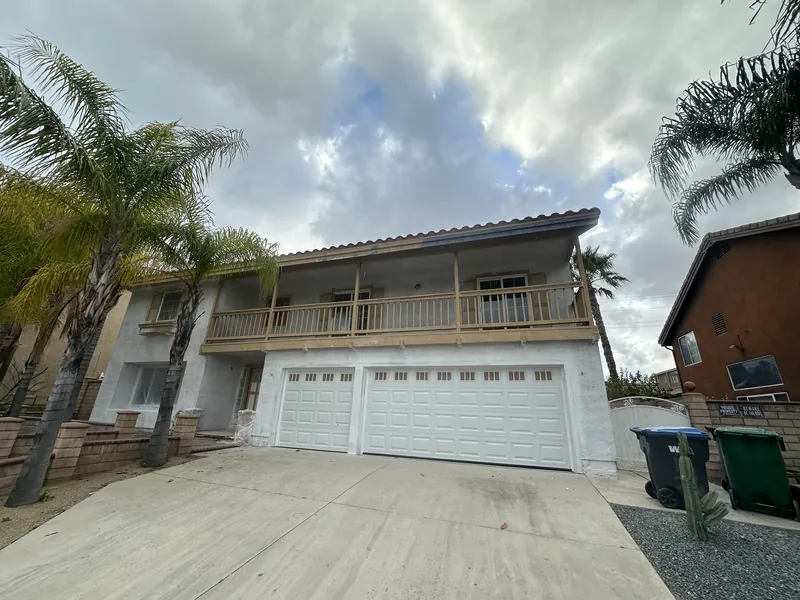 Front of the home mid project with fresh white paint over tan stucco, raw new balcony lumber and white garage doors