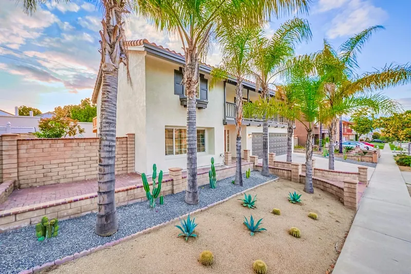 Two-story home after repaint with dark trim, wood balcony, palms and gravel planters of agave and barrel cactus