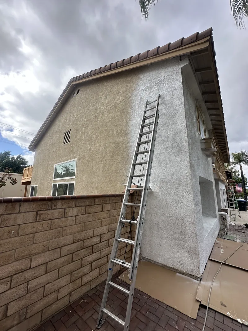 Extension ladder against the gable wall with fresh white paint going over the old tan stucco