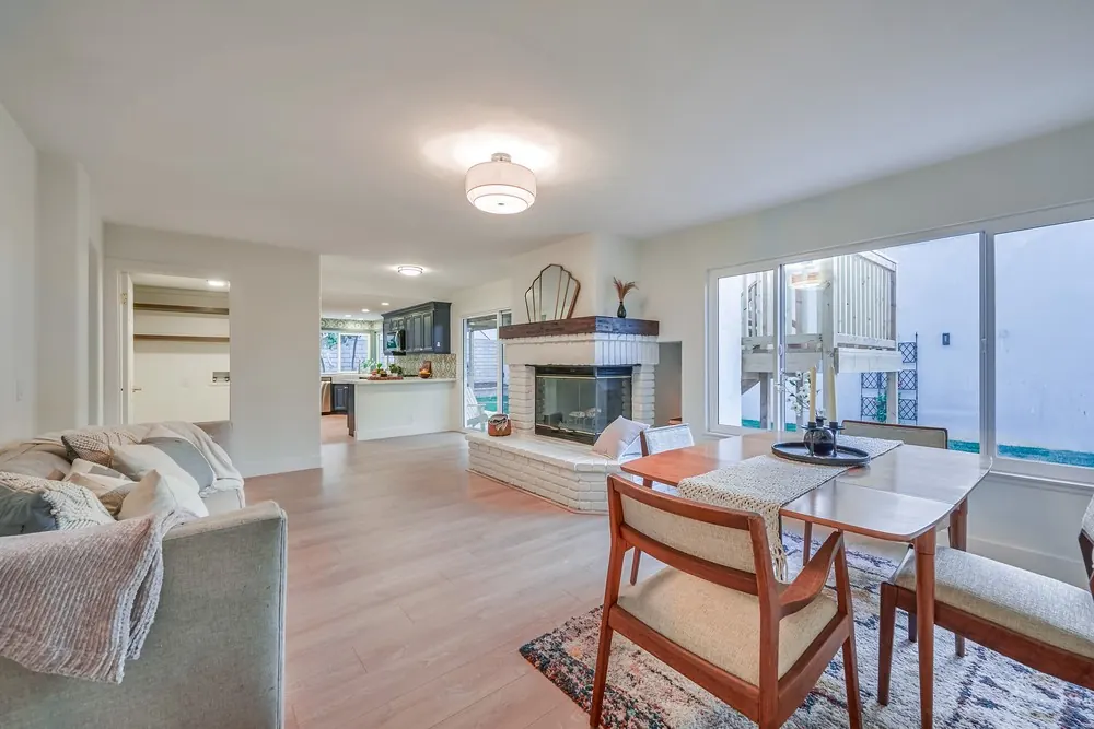 Family room with a white painted brick fireplace, dining table by the windows and the new kitchen open beyond