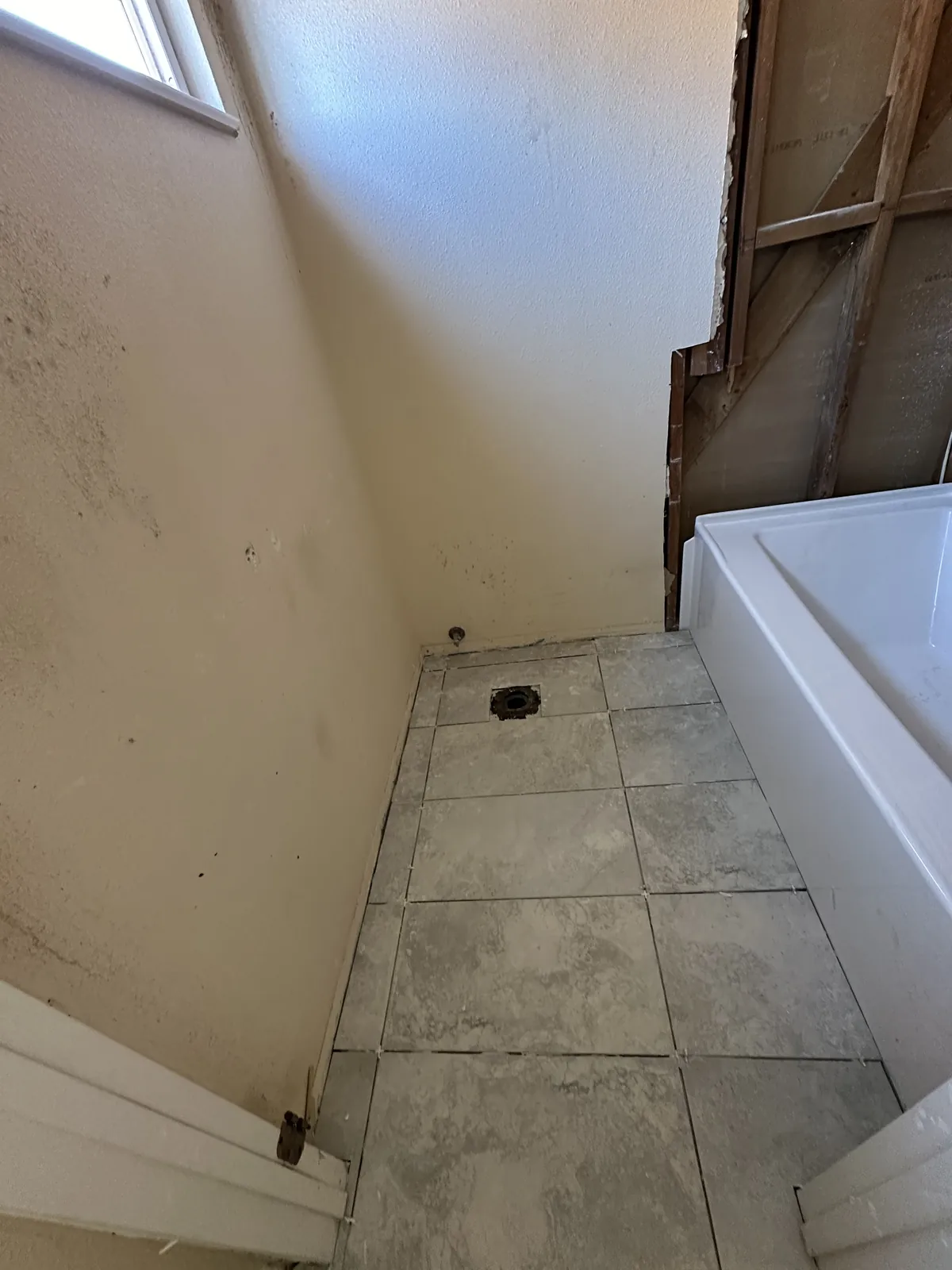 Hall bathroom mid demolition with the toilet removed, wall opened to the framing and the tub still in place