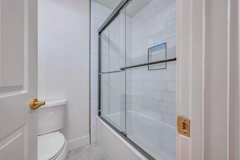 Tub and shower with white subway tile, a recessed niche and a frameless sliding glass door