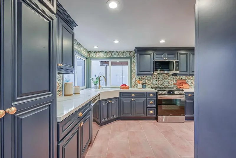 Remodeled kitchen with navy cabinets, brass-tone pulls, white counters, patterned backsplash and terracotta-tone floor tile