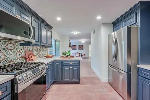 Kitchen range wall with stainless appliances and navy cabinets opening to the dining and family room