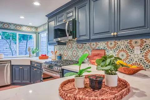Navy raised-panel kitchen with brass-tone hardware, apron-front sink, patterned tile backsplash and white counters