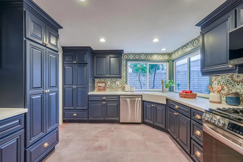 Floor-to-ceiling navy pantry cabinets, dishwasher and corner apron-front sink with terracotta-tone floor tile
