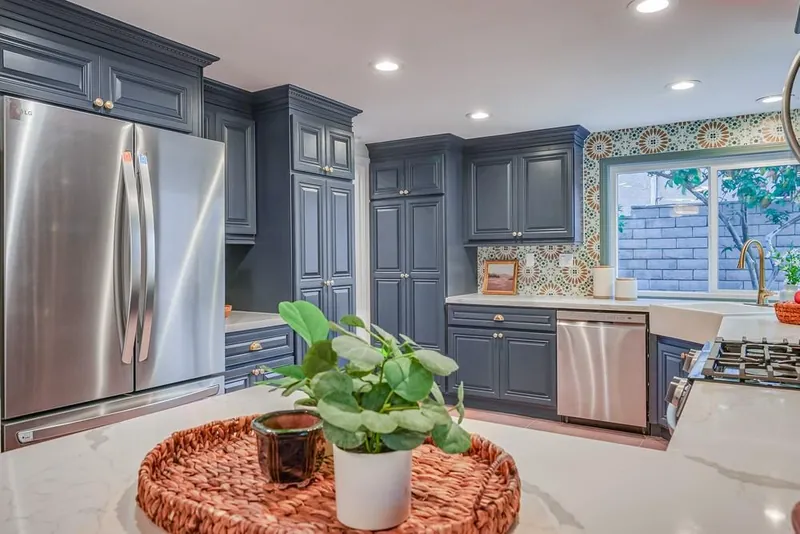 Kitchen with stainless refrigerator, navy pantry cabinets, apron-front sink under the window and white peninsula