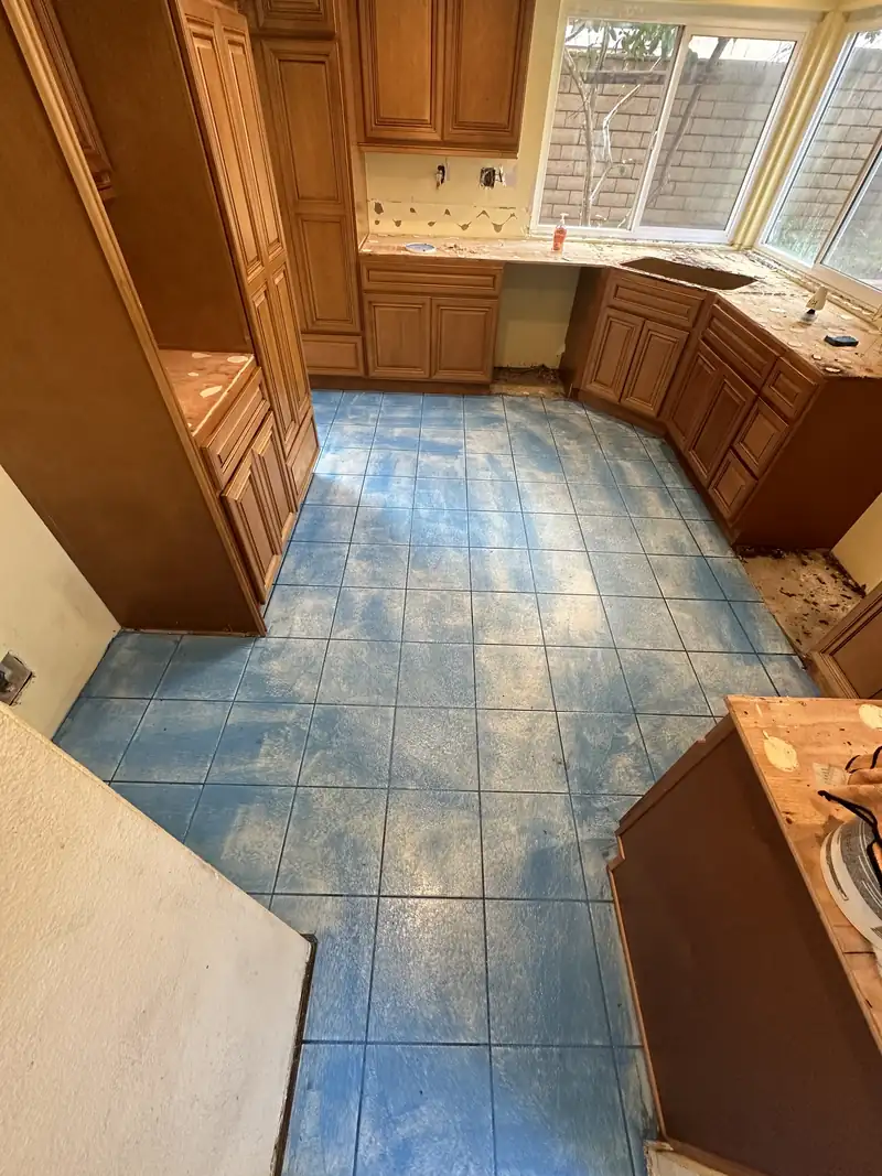 Old kitchen with wood cabinets, stripped countertops and a worn blue tile floor before the remodel