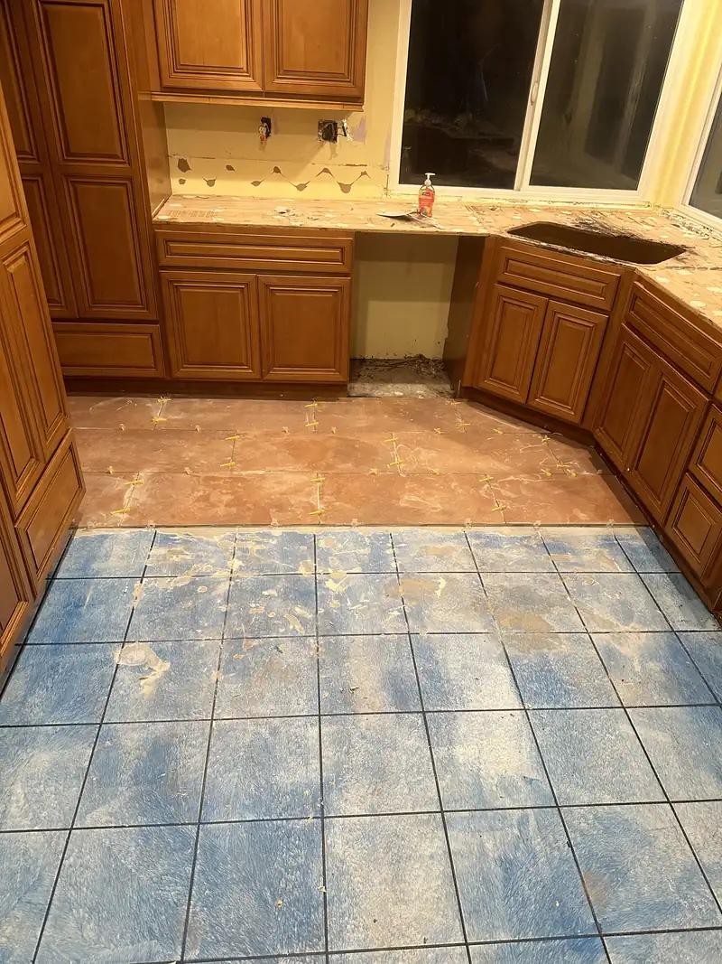 New terracotta-tone floor tile with spacers going down over the old blue kitchen tile beside the original cabinets