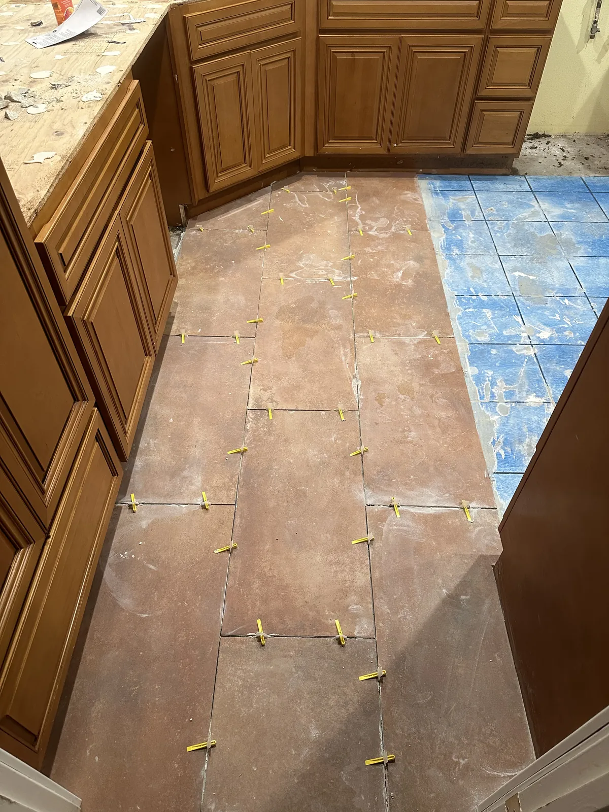 Terracotta-tone floor tile with yellow spacers running between the old wood cabinets and the stripped counter