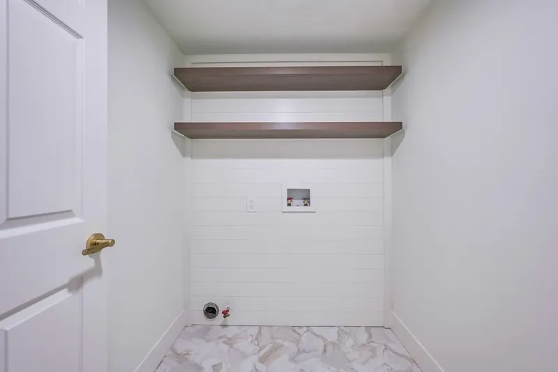 Laundry nook finished with shiplap, two floating wood-tone shelves, new hookups and marble-look floor tile