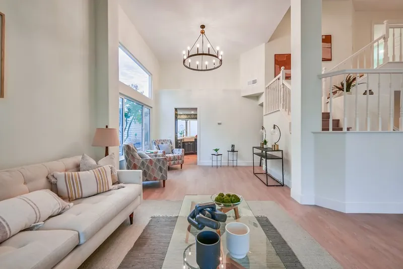 Vaulted living room with a ring chandelier, tall windows, new plank floors and a view through to the navy kitchen