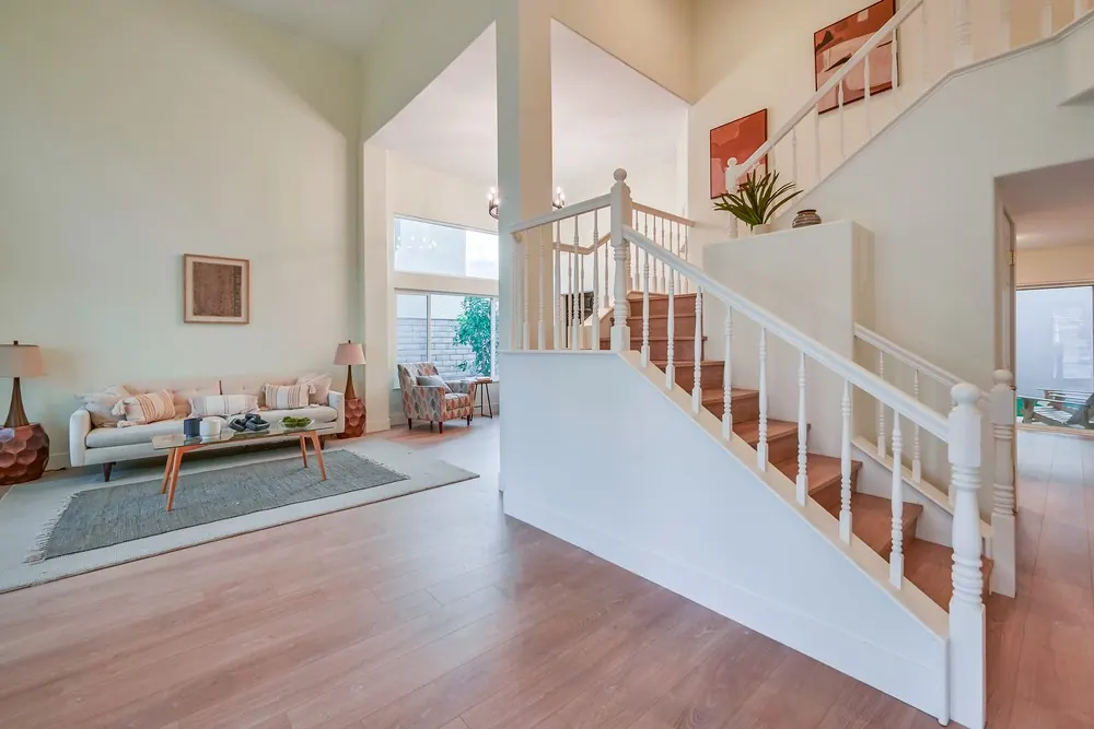 Two-story living room with new light plank flooring, white painted staircase with wood-tone treads and a staged sofa