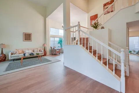 Two-story living room with new light plank flooring, white painted staircase with wood-tone treads and a staged sofa