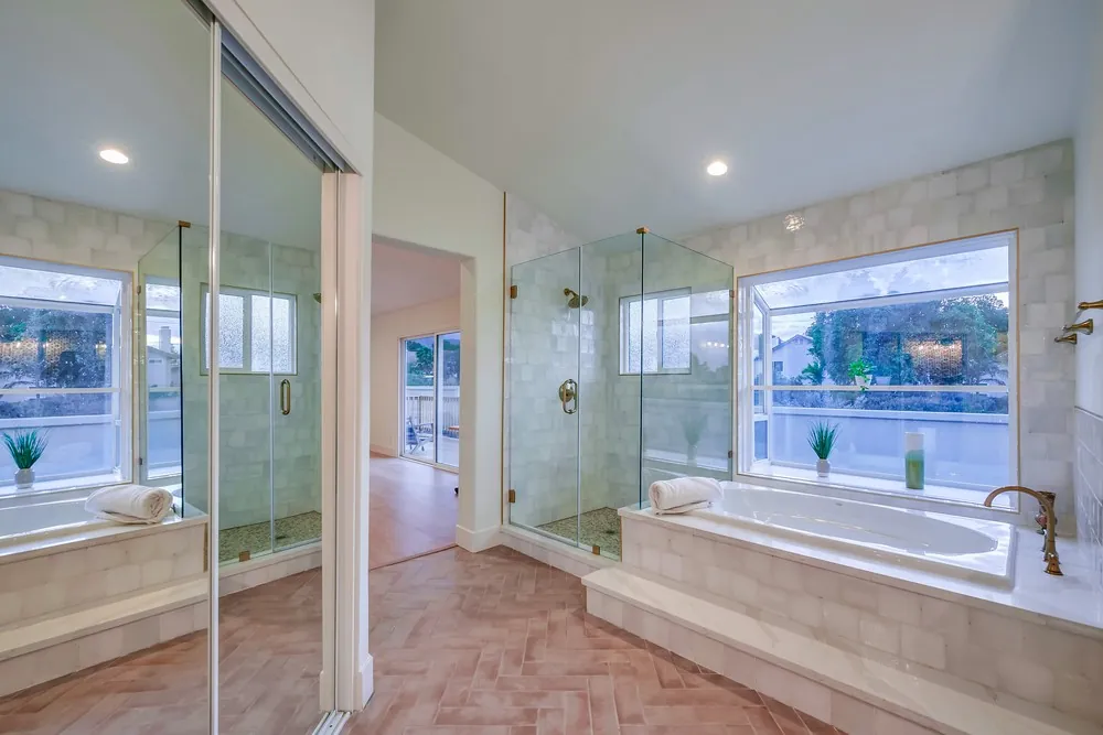Primary bathroom with frameless glass shower, tiled tub deck under a garden window, mirrored closet and herringbone floor