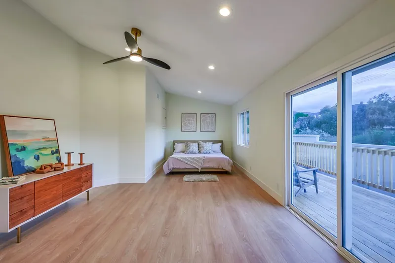 Primary bedroom with vaulted ceiling, new ceiling fan, plank flooring and a sliding door onto the new wood deck