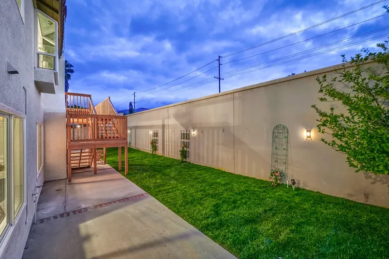 Side yard at dusk with new lawn, concrete path, wall sconces on the block wall and the wood deck stairs beyond