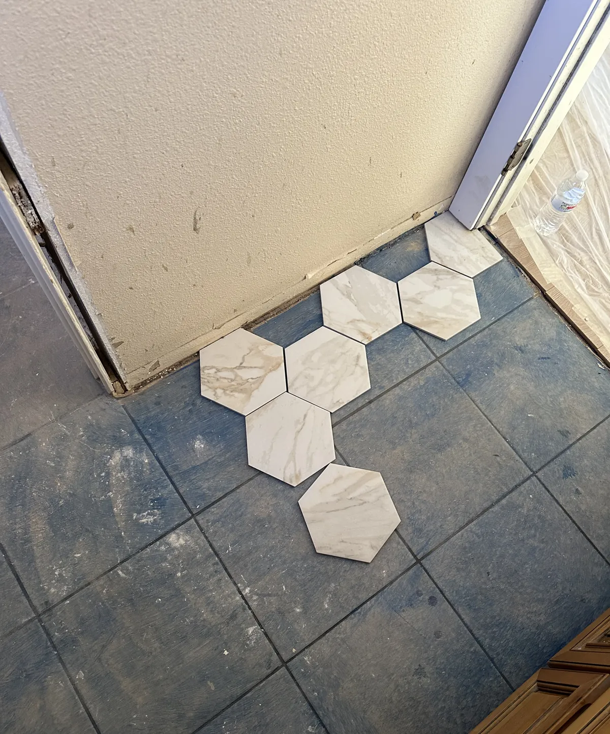 Marble-look hexagon tile samples laid out on the old blue kitchen floor