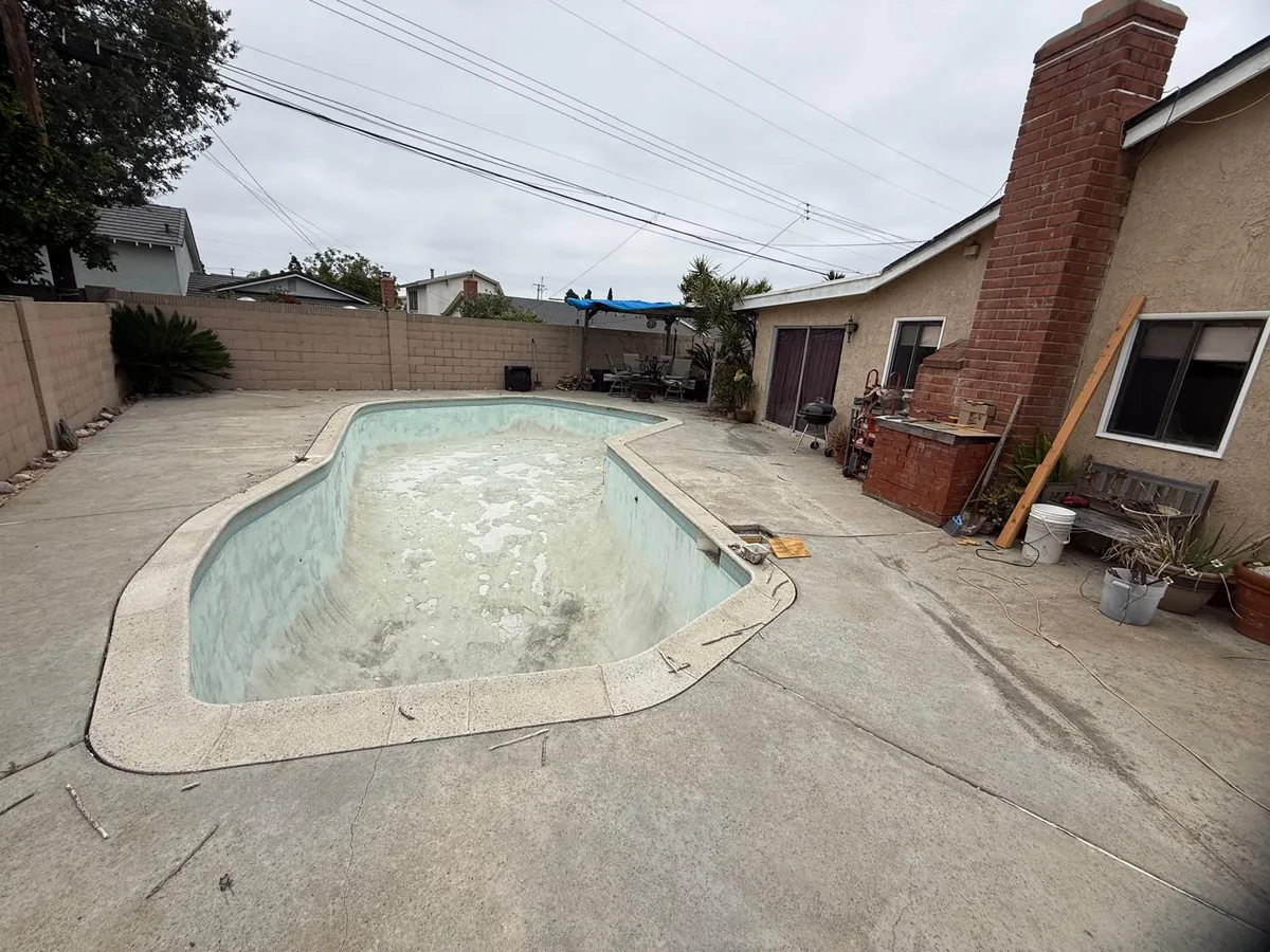 Wide view of the drained backyard pool with old stained plaster, concrete deck and house before the work