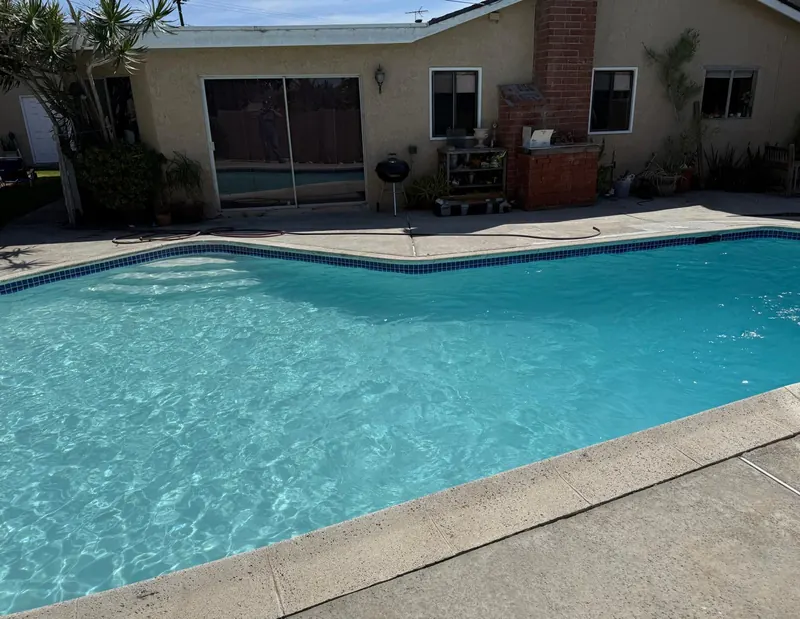 Replastered pool refilled with turquoise water and blue waterline tile in front of the house and brick chimney