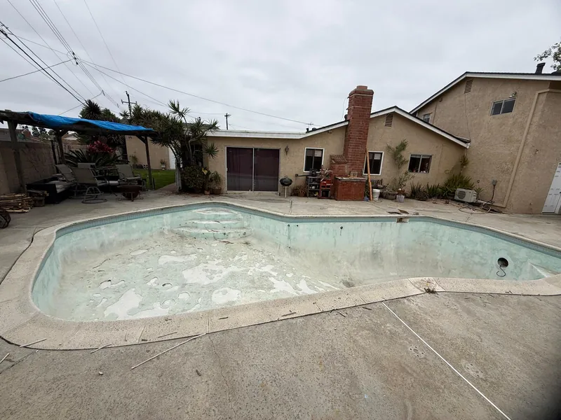 Drained pool with discolored, mottled old plaster and exposed steps in front of the house before replastering