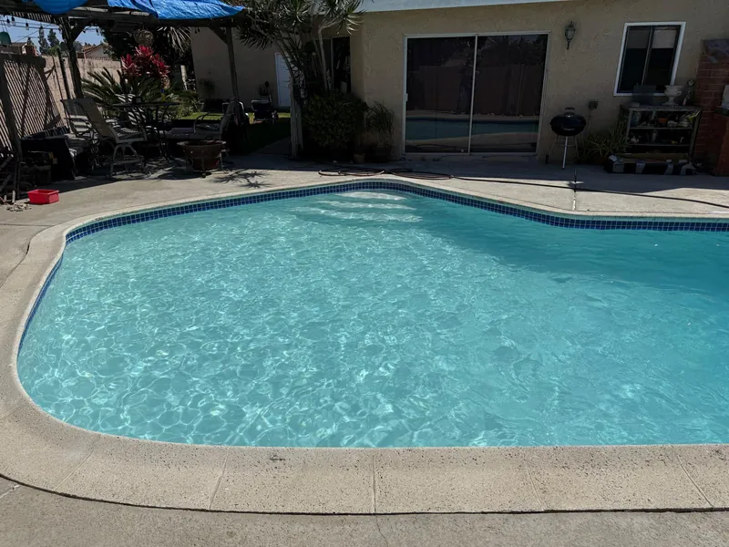 Refilled pool with bright turquoise water and blue waterline tile, seen from the deck toward the house and patio