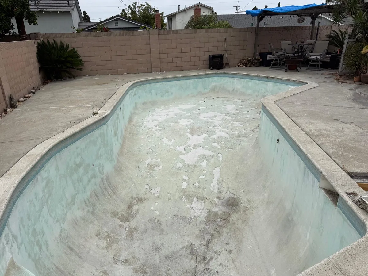 Drained pool with stained, worn plaster and white patches across the floor before replastering