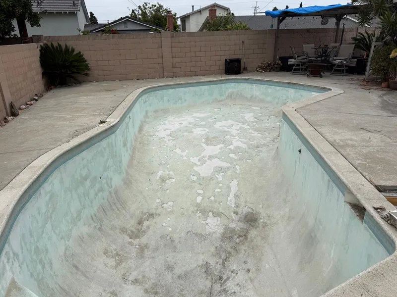 Drained pool with stained, worn plaster and white patches across the floor before replastering