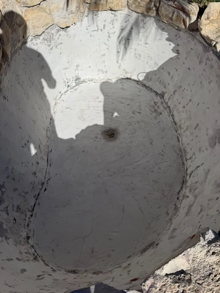 Drained rock fountain basin with old white plaster stained, chipped and cracked around the drain