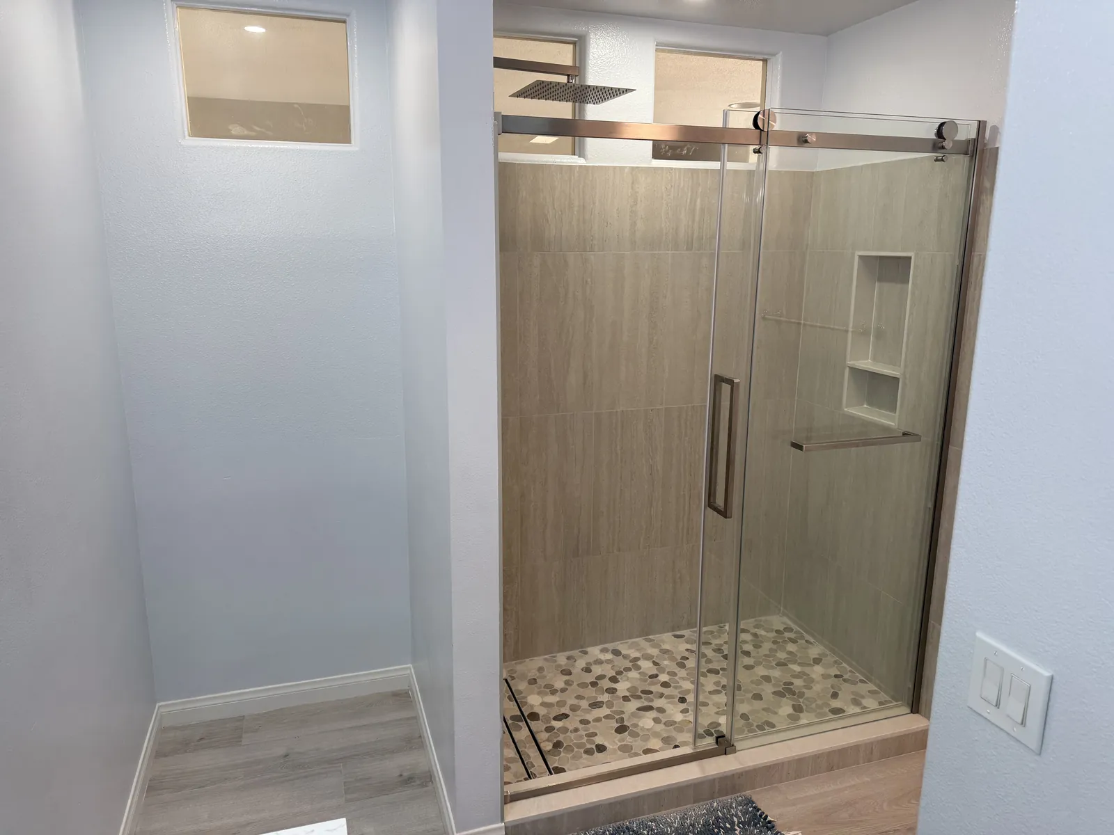 Corner shower with a clear glass door, gray wood-look tile, a recessed niche and a pebble tile floor