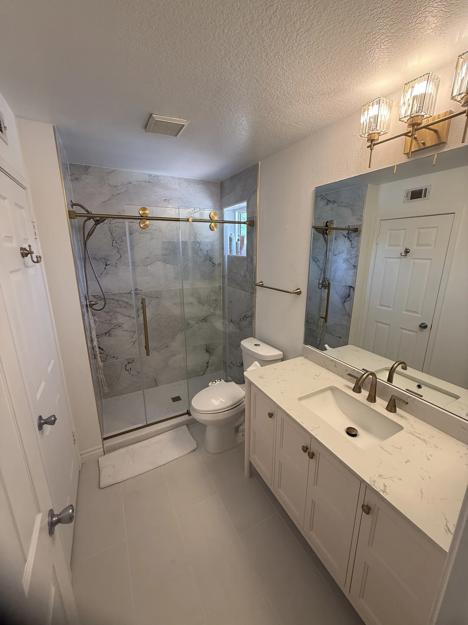 Bathroom with a tub and shower in marble-look tile behind glass, gold fixtures and a white quartz vanity with a gold faucet