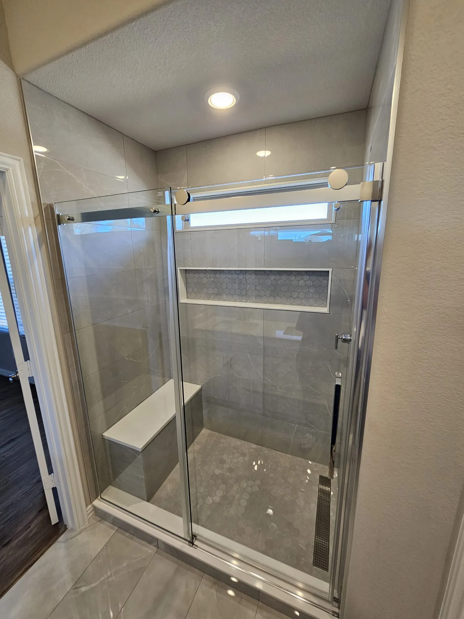 Shower behind sliding glass with light tile, a built-in bench seat and a mosaic tile niche
