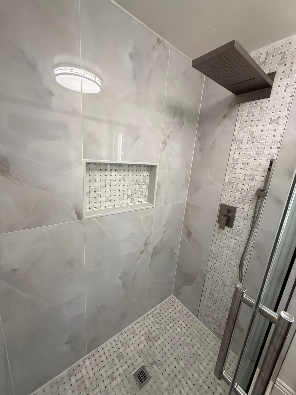 Shower in large gray tile with a mosaic tile niche, a black rain head and a hexagon tile floor