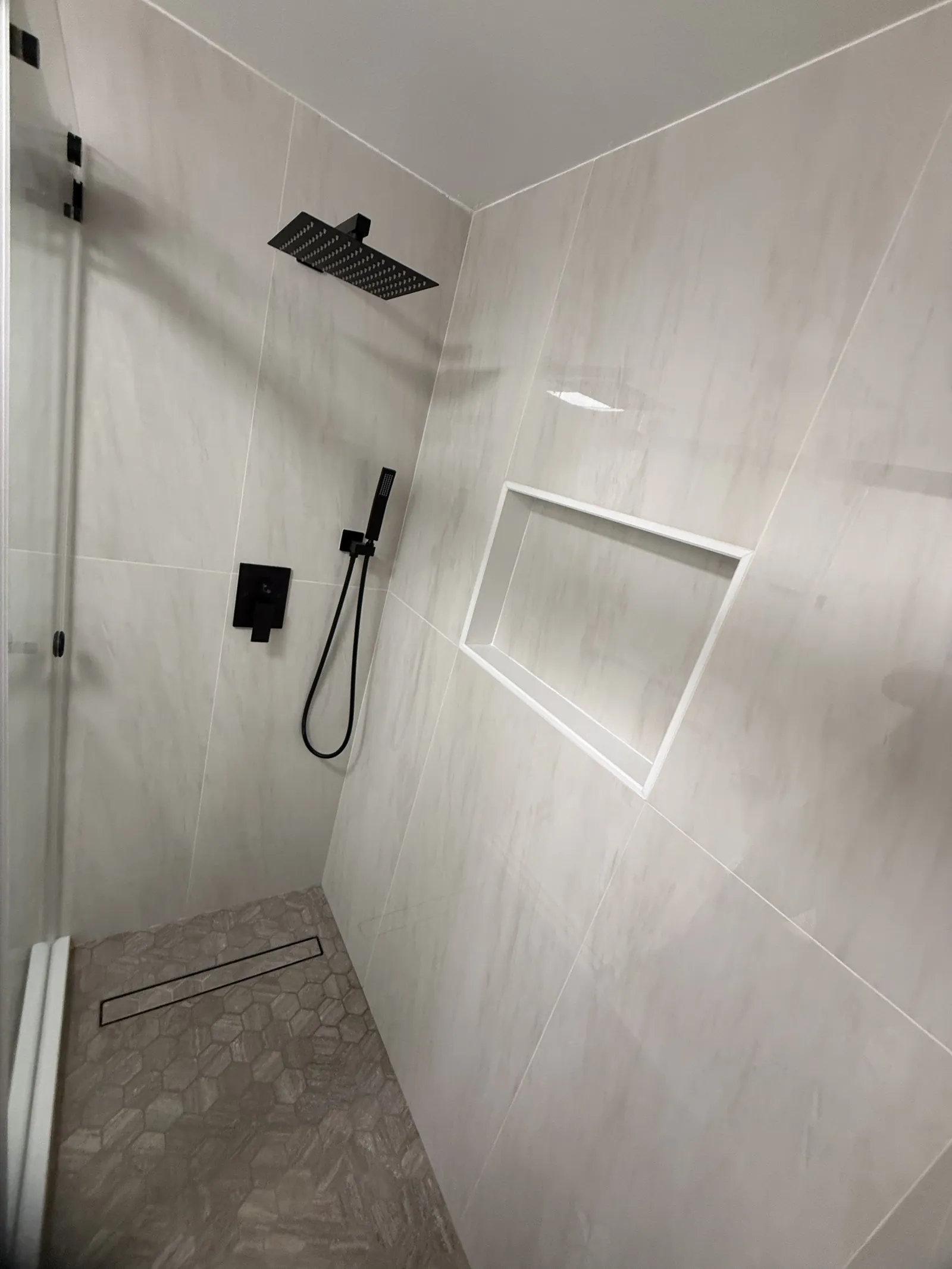 Shower corner in light wood-look tile with a black square rain head, a handheld sprayer and a recessed niche