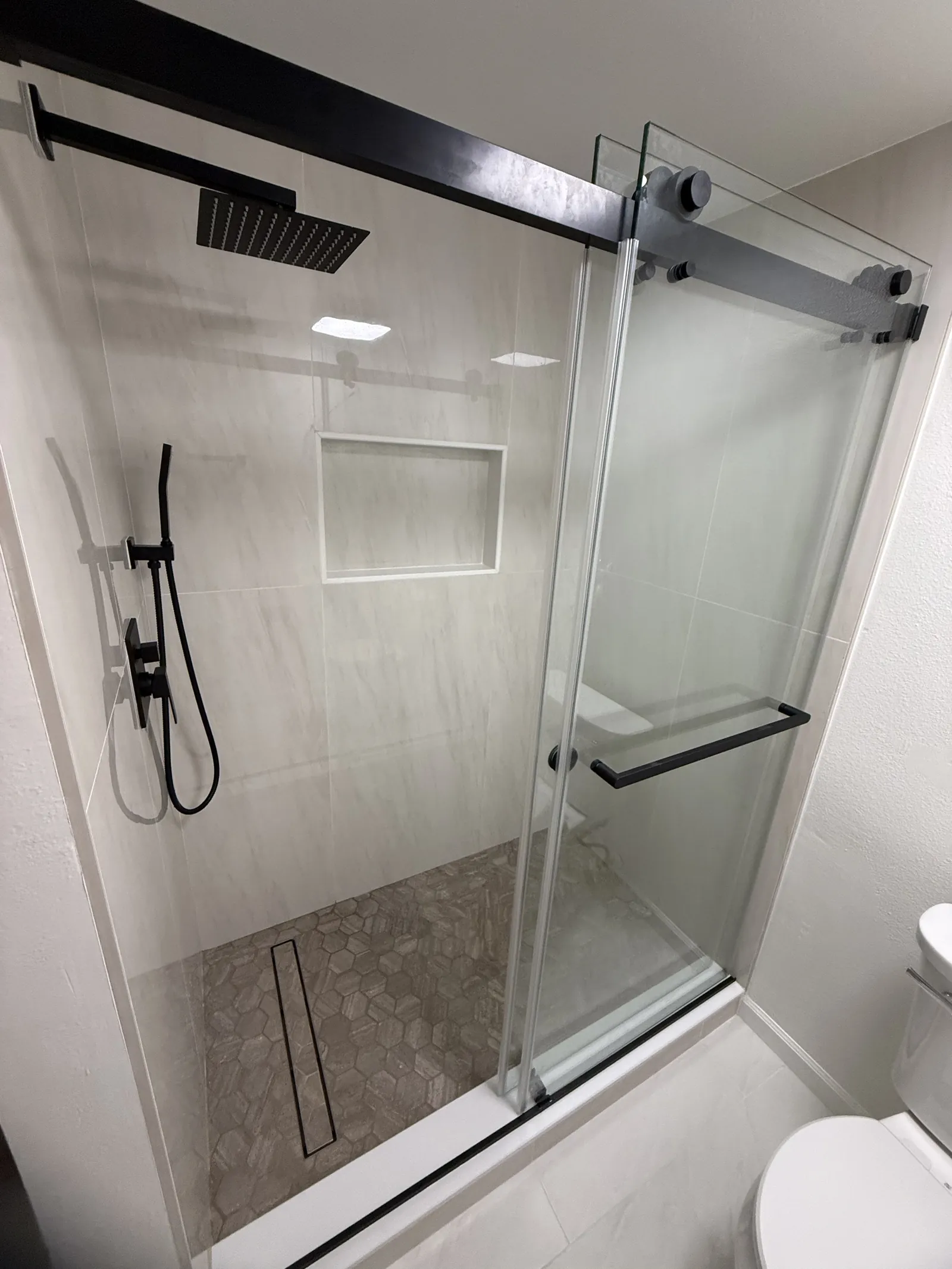 Tub and shower behind sliding glass on black track hardware, light wood-look tile and a long recessed niche