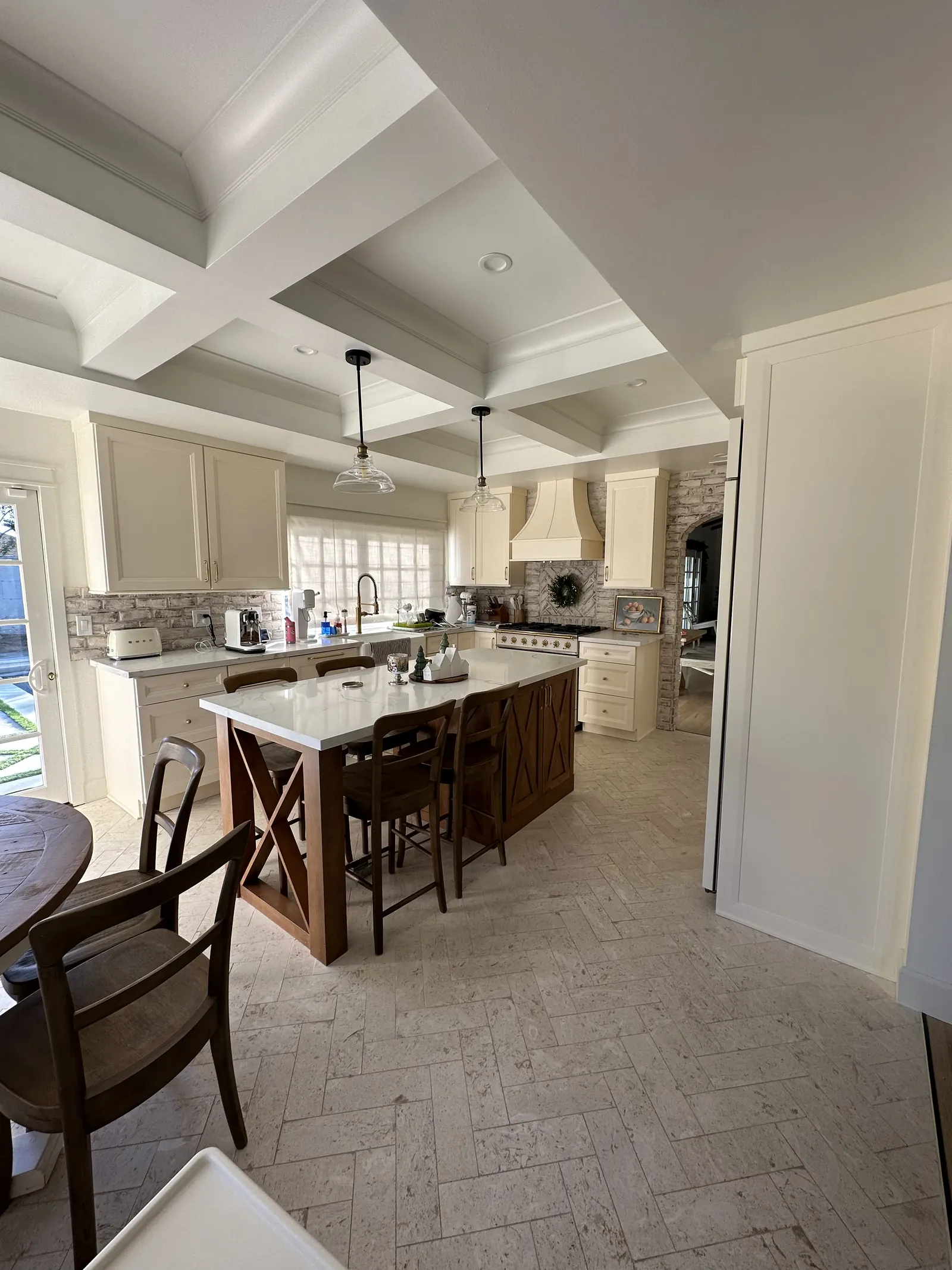Kitchen under a coffered ceiling with an island and stools, dark cabinets and a brick-look tile floor