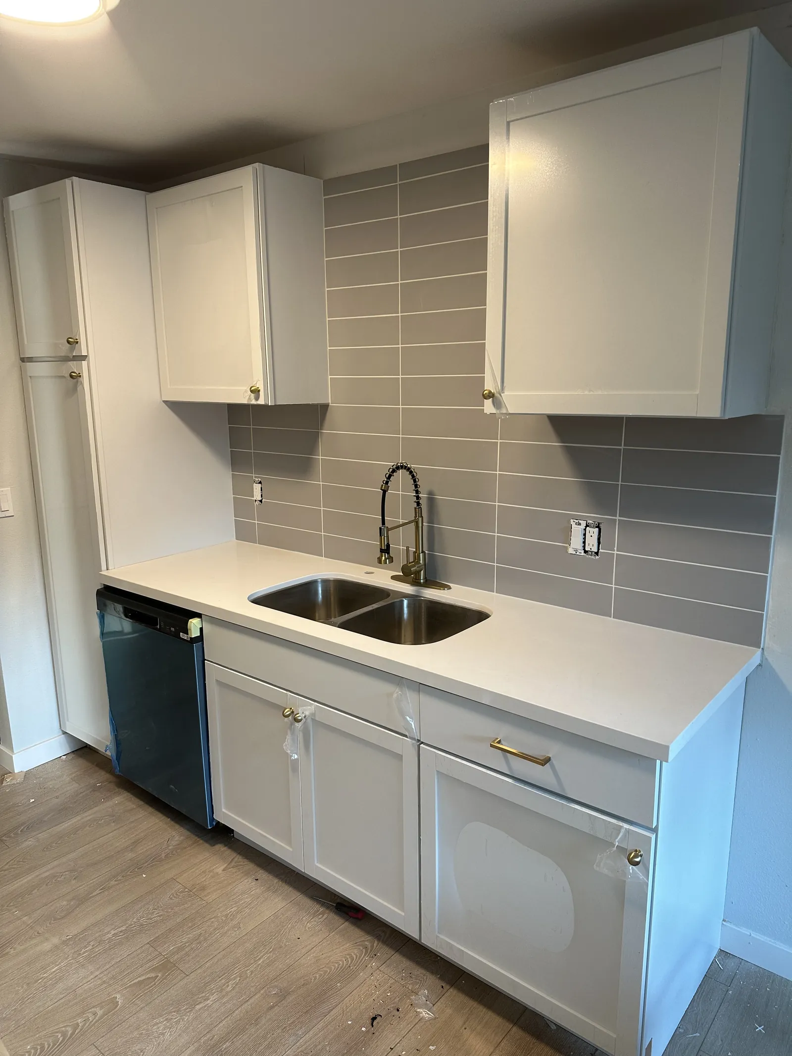 Gray kitchen cabinets with a white quartz counter, a stacked tile backsplash, an undermount sink and a black faucet