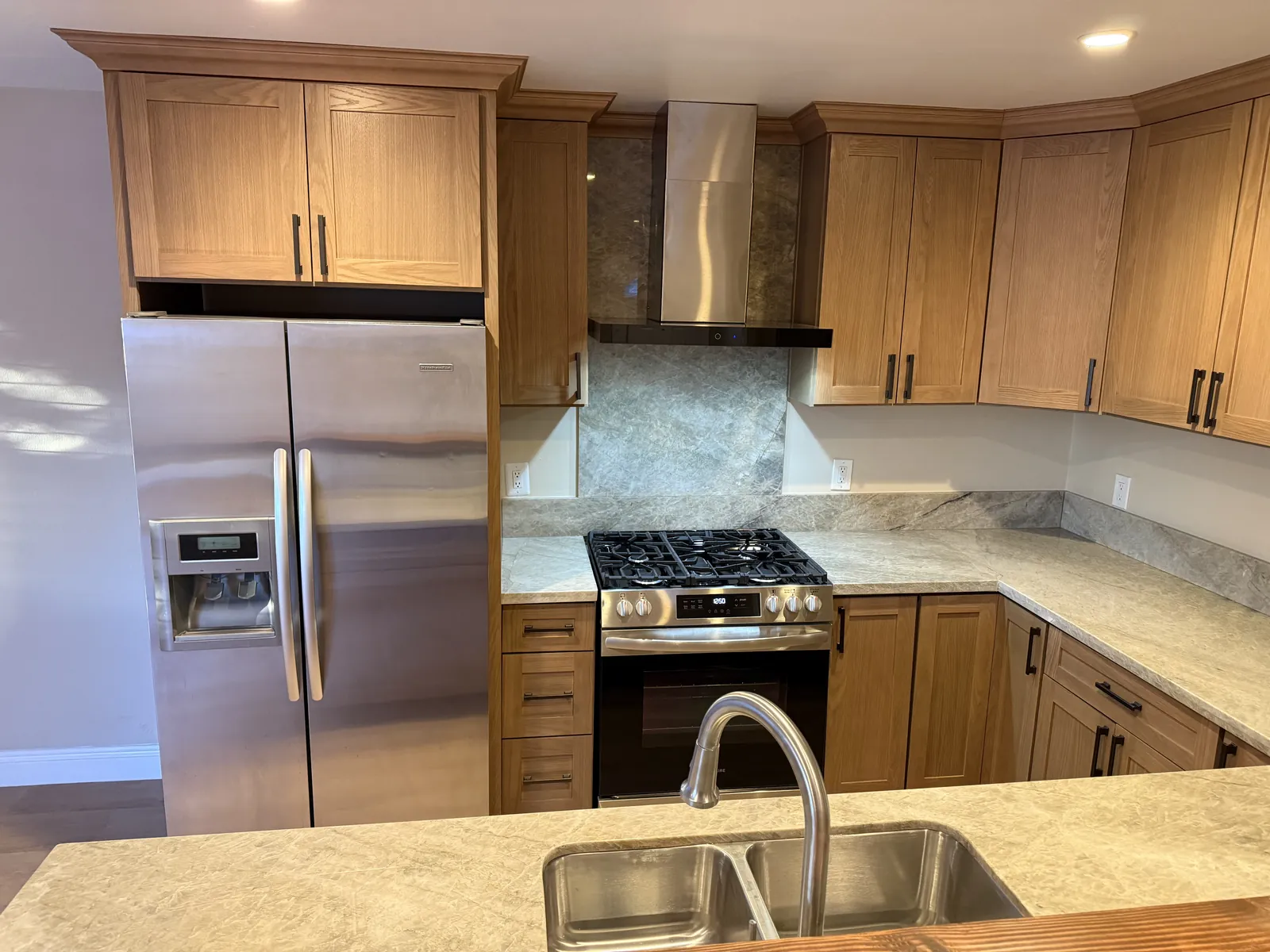 Oak kitchen with a stainless range and wall hood, a stone counter and backsplash and a double sink