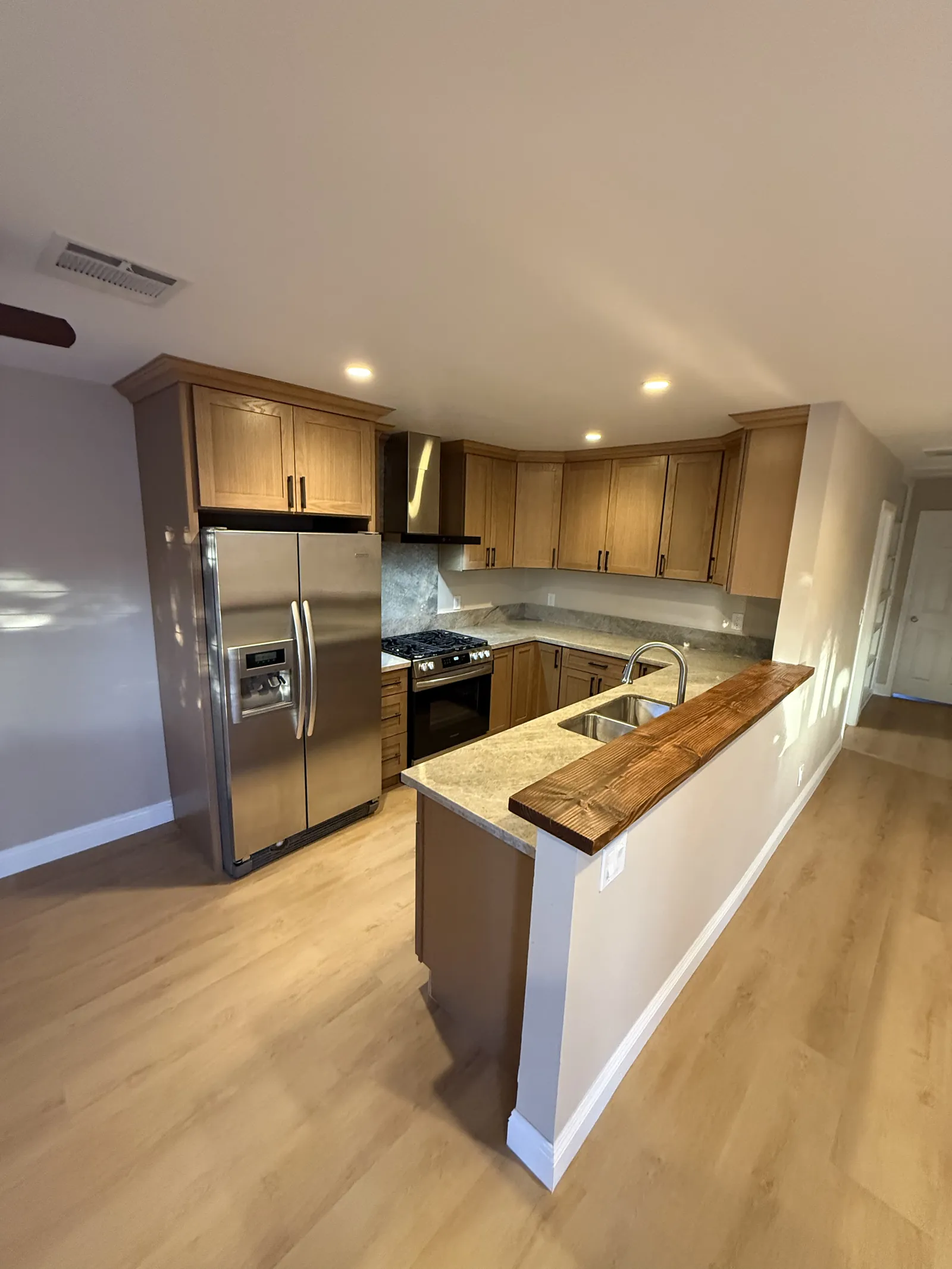 Oak kitchen cabinets with stainless appliances and a stone peninsula finished with a wood edge